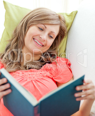 Smiling woman reading a book lying on a sofa