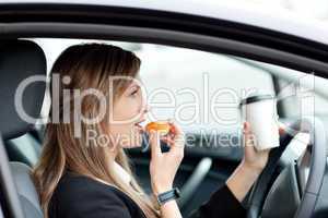 Charming businesswoman eating and holding a drinking cup while d