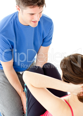 Brunette woman doing sit-ups assited by her personal trainer