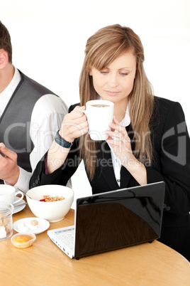 Serious businesswoman using a laptop while having breakfast