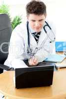 Assertive male doctor using a laptop sitting at his desk