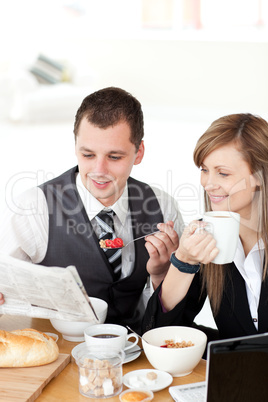 Smiling couple of business people reading a newspaper while havi