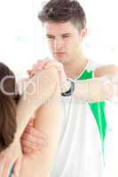 Concentrated physical therapist checking a woman's shoulder
