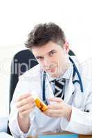 Serious male doctor holding pills sitting at his desk
