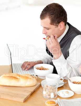 Charming businessman using a laptop while having breakfast