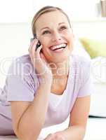 Delighted woman talking on phone lying on the floor