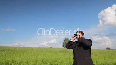 Business man in a field look into binoculars