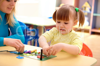 Teacher and little girl play with plasticine