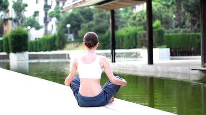 Woman meditating by the water in the park