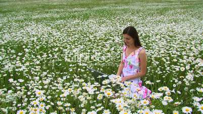 A girl sits on a field with a computer