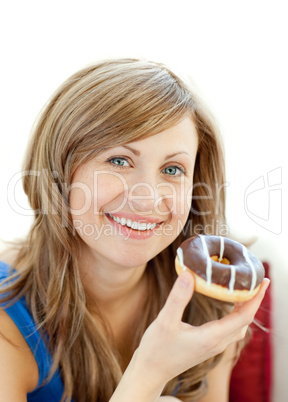 Delighted woman is eating a donut on a sofa