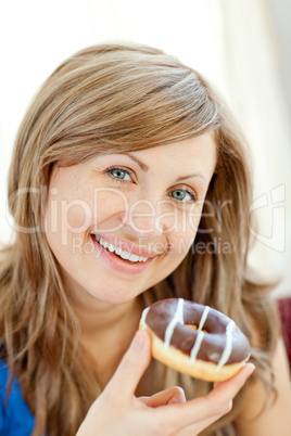 Smiling woman is eating a donut on a sofa