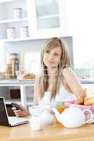 Cheerful woman using a phone and laptop in the kitchen