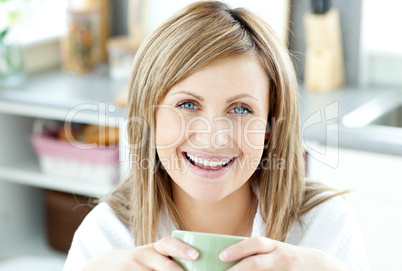 Cheerful woman holding a cup of tea in the kitchen