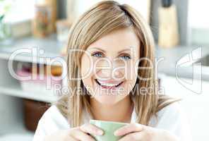 Cheerful woman holding a cup of tea in the kitchen