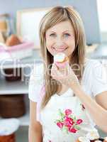 Delighted woman eating a little cake in the kitchen