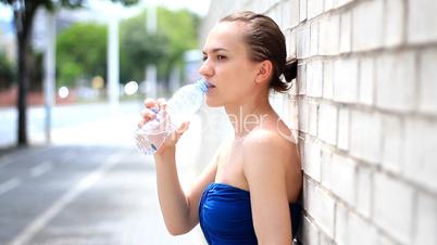 Woman stands against the wall and drinking water