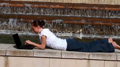 Woman with laptop lying near the fountain