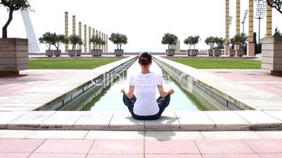 Woman meditating by the water in the park