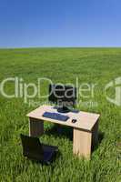 Desk and Computer In Green Field With Blue Sky