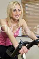 Beautiful Young Blond Woman on Exercise Bicycle at Gym