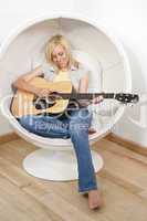 Beautiful Young Blond Woman Playing Guitar in Bubble Chair