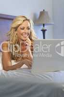 Beautiful Happy Blond Woman Using White Laptop Computer In Bed