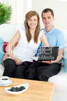 Cheerful couple using a laptop sitting on a sofa