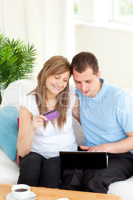 Smiling couple shopping on-line sitting on a sofa