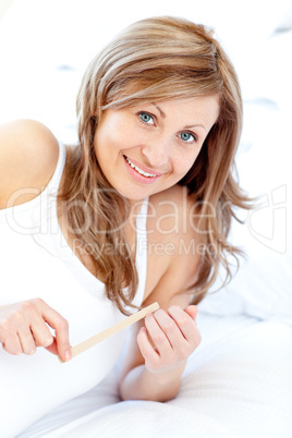 Bright woman using a nail file lying on her bed