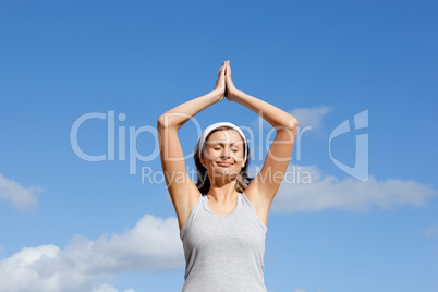Cheerful woman meditating against a blue sky
