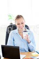 Smiling businesswoman holding a coffee while using a laptop