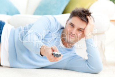 Smiling young man holding a remote lying on the floor
