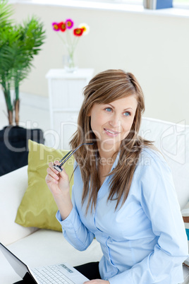 Radiant woman using a laptop sitting on a sofa