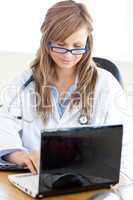 Confident female doctor using a laptop sitting at her desk