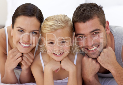 Cute little girl with her parents lying on a bed