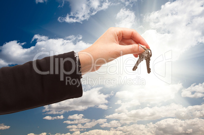 Female Holding Out Pair of Keys Over Clouds and Sky