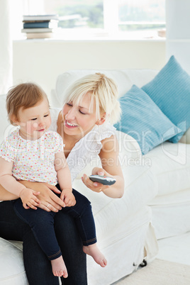 Jolly woman using a remote with her girl in the living-room