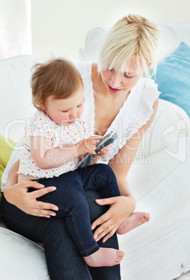 Blond woman using a remote with her girl in the living-room