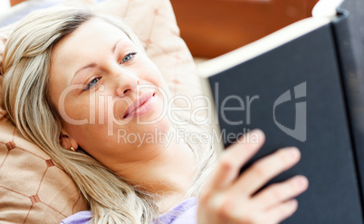 Radiant woman lies on sofa and reading a book