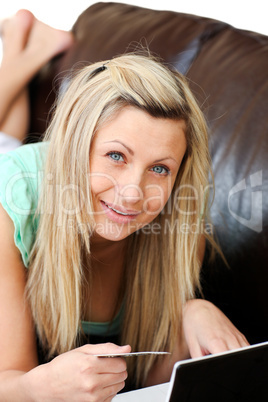 Attractive woman lies on sofa and works at laptop