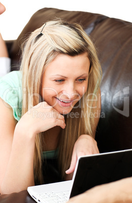 Smiling woman lies on sofa and works at laptop