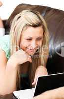 Smiling woman lies on sofa and works at laptop