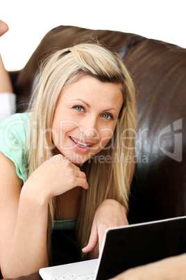 Cute woman lies on sofa and works at laptop