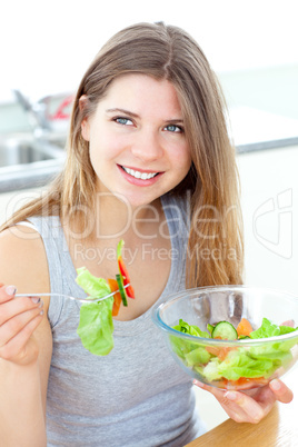 Smilling woman eating salad in the kitchen