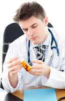 Serious male doctor holding pills sitting at his desk