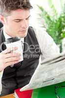 Charismatic businessman drinking a coffee while reading a newspa