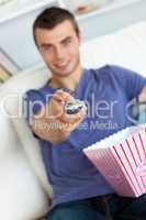 Smiling man is relaxing in the living-room with popcorn