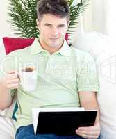 Joyful young man holding a cup of coffee and a laptop