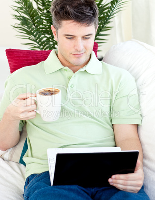Smiling young man holding a cup of coffee looking at a laptop